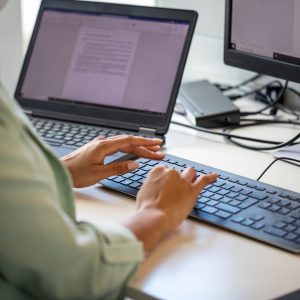 Close-up of woman typing on computer keyboard at workplace. Businesswoman using desktop computer in office.